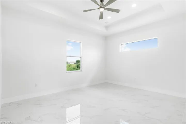 Tiled spare room with ceiling fan, a raised ceiling, and plenty of natural light