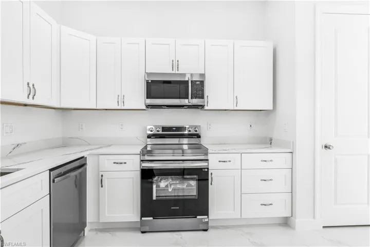 Kitchen featuring light tile patterned floors, appliances with stainless steel finishes, light stone counters, and white cabinetry