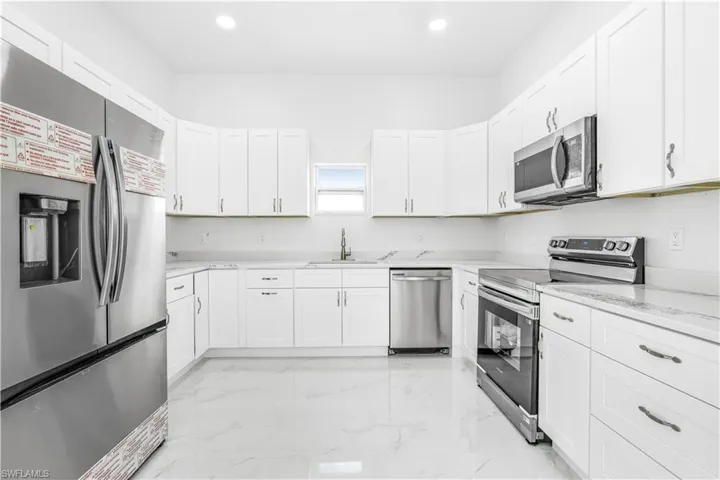 Kitchen with appliances with stainless steel finishes, white cabinets, light stone counters, and sink