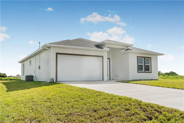 View of front of house featuring a garage, cooling unit, and a front yard