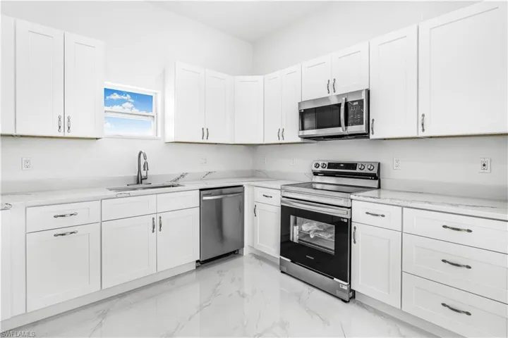 Kitchen with light tile patterned floors, stainless steel appliances, sink, and white cabinetry