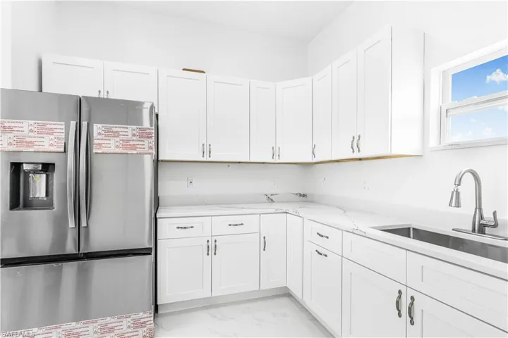 Kitchen with white cabinetry, light stone countertops, stainless steel fridge, light tile patterned floors, and sink
