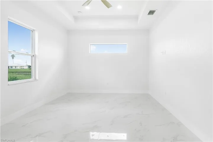 Tiled empty room with ceiling fan, a raised ceiling, and plenty of natural light