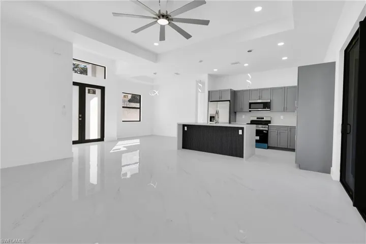 Kitchen featuring open floor plan, a kitchen island, appliances with stainless steel finishes, light marble finish floors, and a tray ceiling