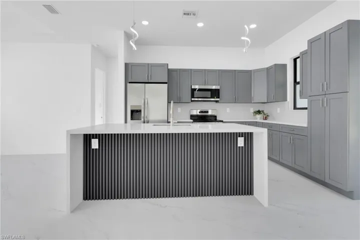 Kitchen featuring light marble finish flooring, gray cabinetry, stainless steel appliances, light stone countertops, and recessed lighting