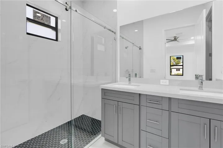 Bathroom with double vanity, a marble finish shower, and a ceiling fan