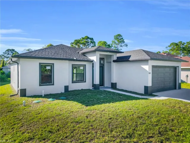 View of front of house with an attached garage, stucco siding, a front lawn, and driveway