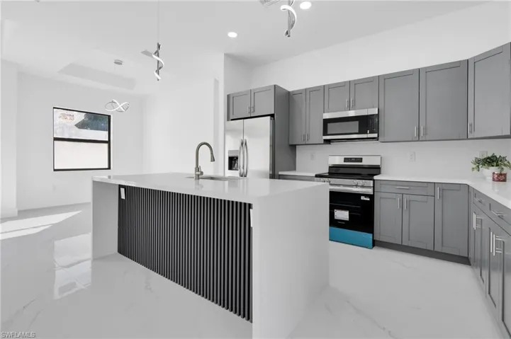 Kitchen with light marble finish flooring, gray cabinetry, stainless steel appliances, light stone counters, and hanging light fixtures