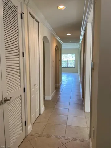 Hall with arched walkways, recessed lighting, crown molding, and light tile patterned floors