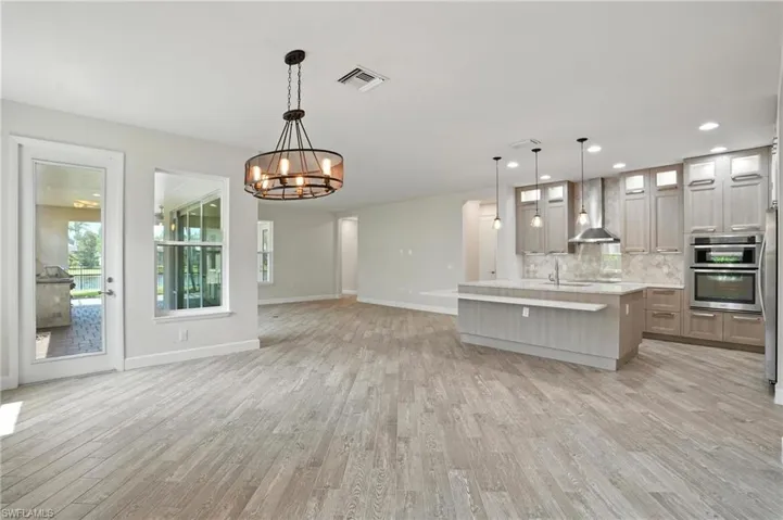 Kitchen featuring light countertops, light wood-style floors, backsplash, a chandelier, and wall chimney range hood