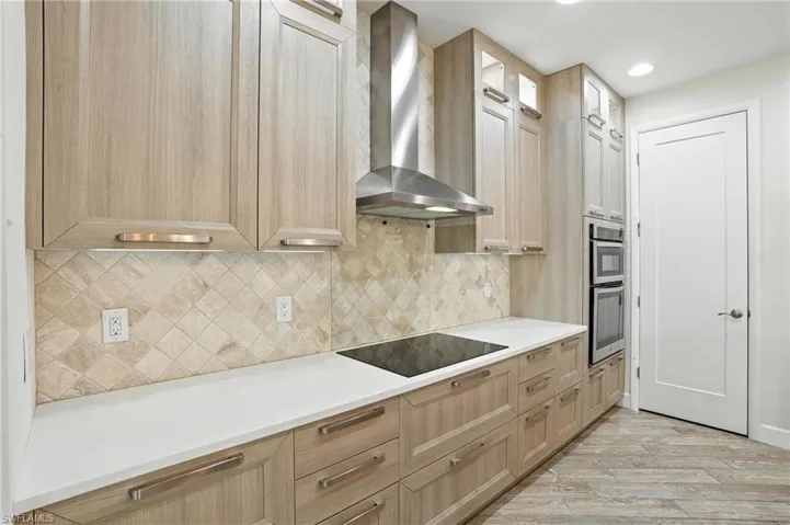 Kitchen featuring wall chimney exhaust hood, light wood-style flooring, light brown cabinetry, black electric cooktop, and recessed lighting