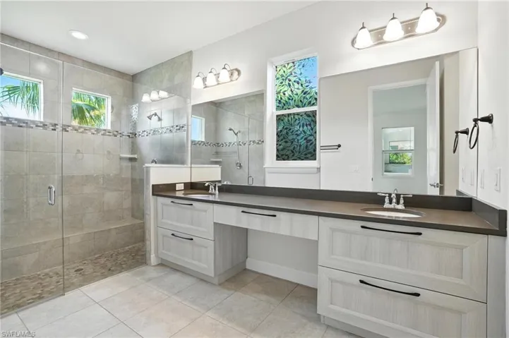 Full bath featuring a stall shower, double vanity, and tile patterned flooring
