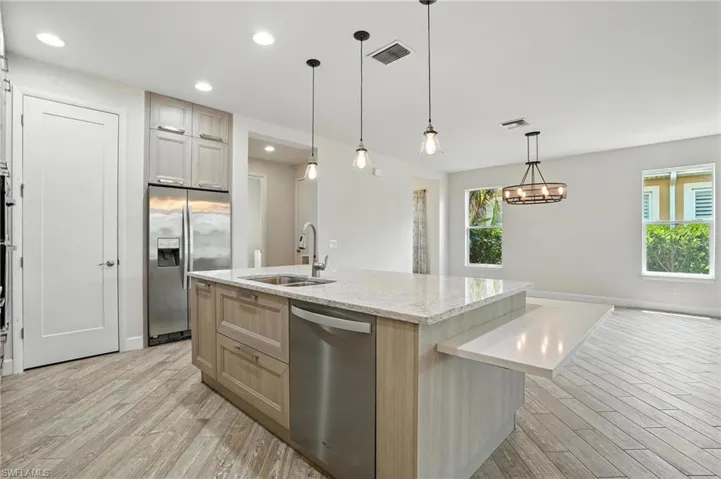Kitchen featuring light wood finished floors, appliances with stainless steel finishes, an island with sink, light brown cabinetry, and light stone countertops
