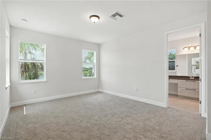 Unfurnished bedroom featuring light carpet, multiple windows, and connected bathroom