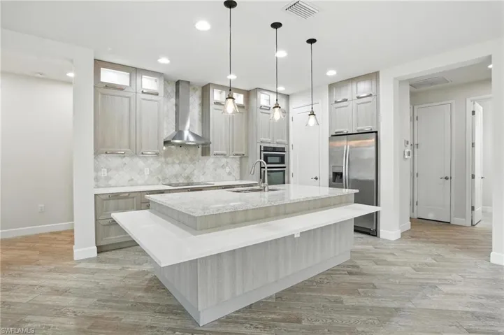 Kitchen with appliances with stainless steel finishes, an island with sink, tasteful backsplash, recessed lighting, and wall chimney range hood