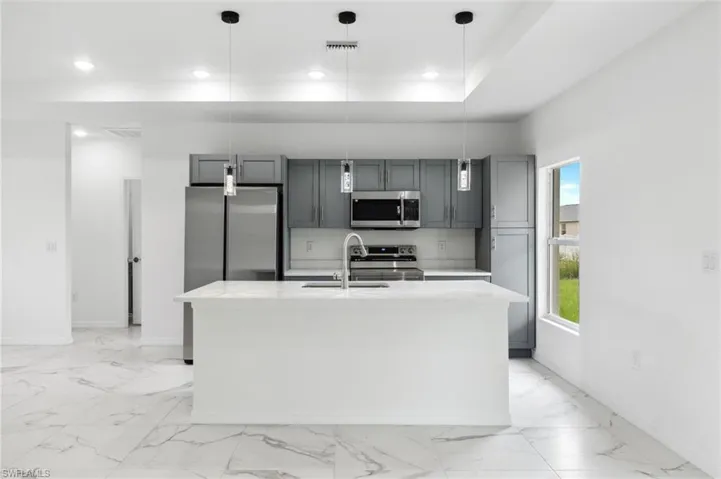 Kitchen with decorative light fixtures, a center island with sink, appliances with stainless steel finishes, sink, and gray cabinets