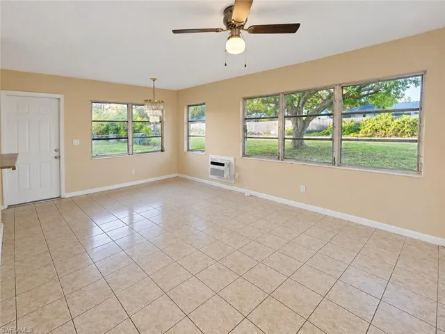Neutral-toned interior space featuring light-colored ceramic tile flooring, large multi-pane windows, a central ceiling fan with integrated lighting, and a wall-mounted air conditioning unit