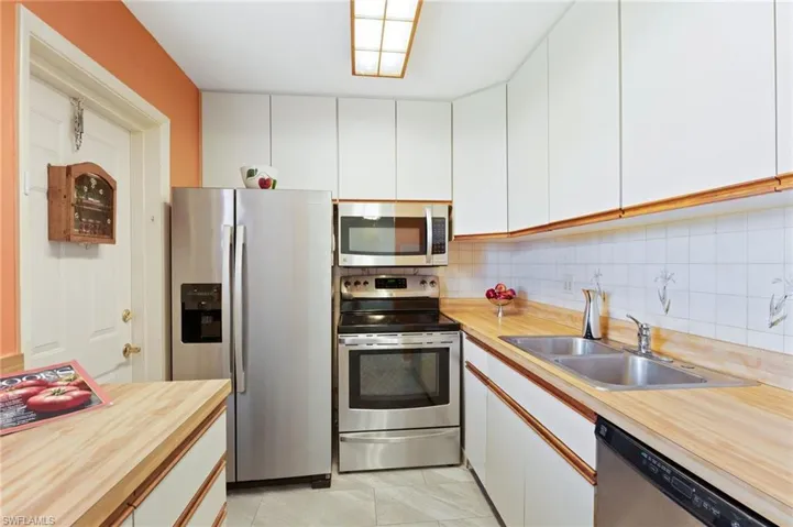 Kitchen featuring stainless steel appliances, light tile patterned flooring, sink, white cabinets, and decorative backsplash