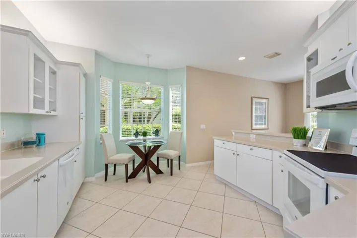 Kitchen with hanging light fixtures, white appliances, white cabinetry, and light tile floors
