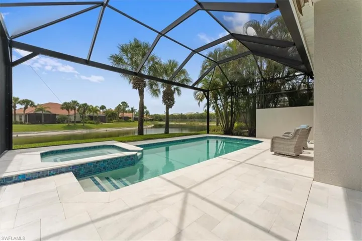 View of swimming pool with a patio area, a water view, a pool with connected hot tub, and glass enclosure