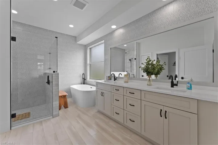 Bathroom featuring a stall shower, double vanity, a freestanding bath, wood finished floors, and recessed lighting
