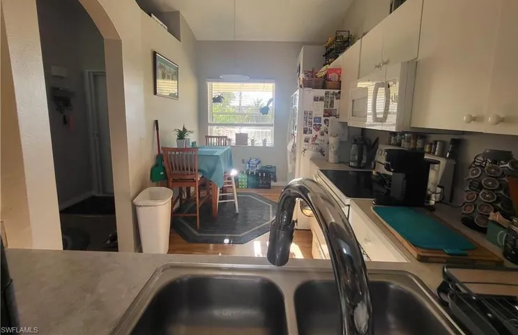 Kitchen featuring white microwave, light countertops, arched walkways, and white cabinets