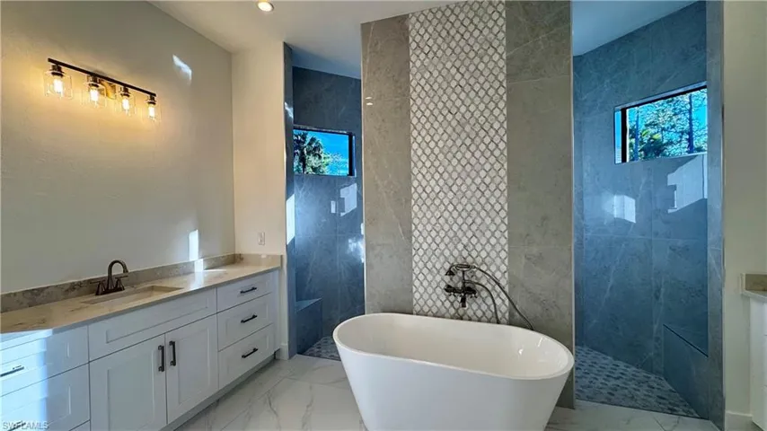 Full bathroom with vanity, walk in shower, light marble finish floors, a freestanding tub, and tile walls