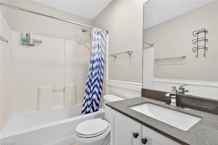 Full bath with a wainscoted wall, shower / bathtub combination with curtain, and vanity
