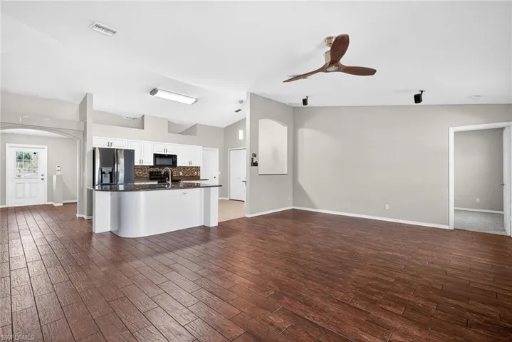 Unfurnished living room with ceiling fan, dark wood-style flooring, lofted ceiling, and arched walkways