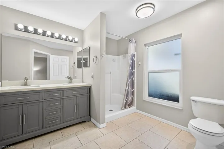 Bathroom with double vanity, a shower stall, and light tile patterned floors