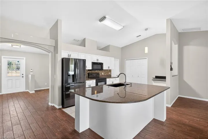 Kitchen featuring arched walkways, dark stone countertops, black appliances, dark wood-style flooring, and lofted ceiling