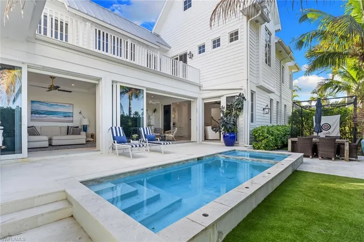 Back of house with a patio area, outdoor dining area, a metal roof, a balcony, and a pool with connected hot tub