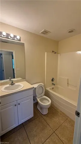 Bathroom featuring a vanity with an integrated sink, a full bathtub with shower, a toilet, tile flooring, and a vanity light fixture