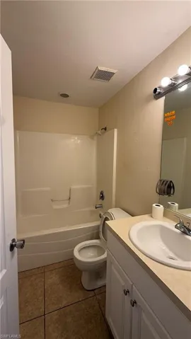 Full bathroom featuring a white tub/shower combination, a toilet, a vanity with a white sink, and tiled flooring