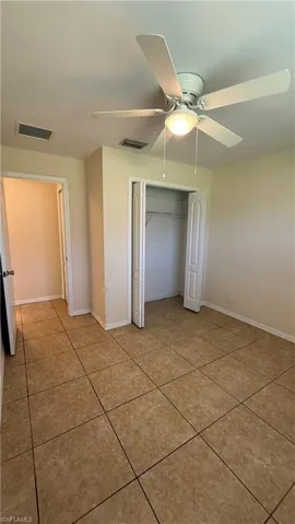 Spacious interior featuring neutral-toned tile flooring, light cream wall paint, and a ceiling fan with integrated lighting
