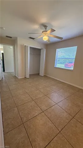 Room featuring large format tile flooring, a ceiling fan with integrated lighting, a window with horizontal blinds, and a bi-fold door closet