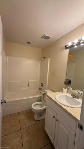 Bathroom featuring a white vanity with built-in sink, a large mirror with Hollywood-style lighting, a toilet, a white shower/tub combination, and tiled flooring