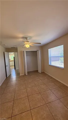Spacious room featuring tile flooring, a ceiling fan with integrated lighting, a louvered bi-fold closet, and a window with horizontal blinds