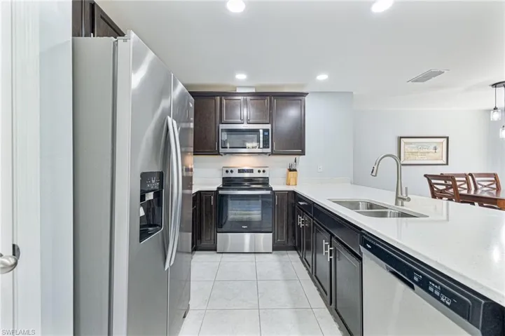 Kitchen featuring light tile patterned flooring, pendant lighting, sink, stainless steel appliances, and dark brown cabinets