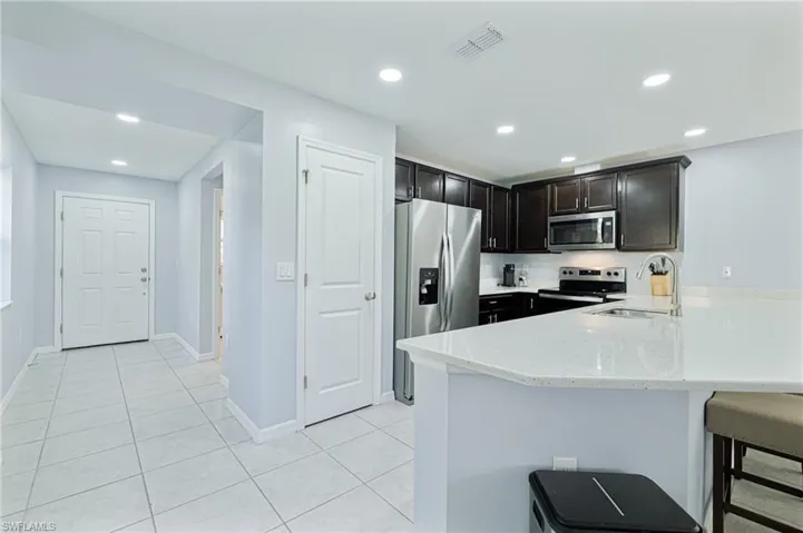 Kitchen with sink, light tile patterned floors, appliances with stainless steel finishes, a kitchen bar, and kitchen peninsula