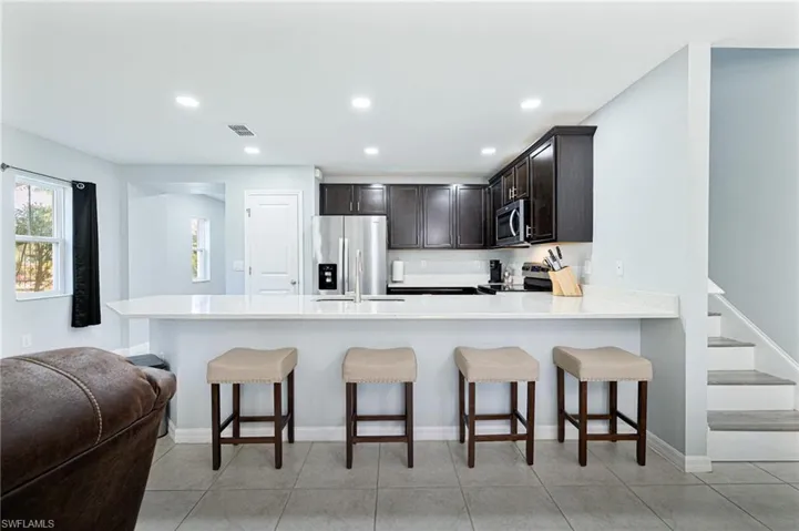 Kitchen with light tile patterned floors, a breakfast bar, appliances with stainless steel finishes, dark brown cabinetry, and kitchen peninsula
