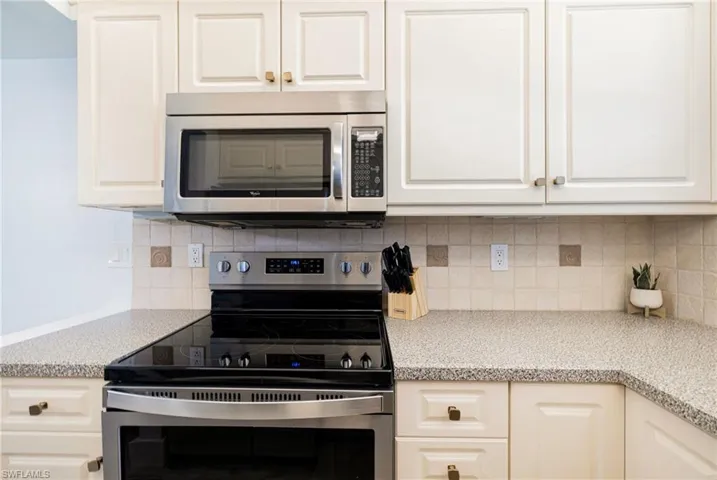 Kitchen featuring stainless steel appliances, decorative backsplash, light stone counters, and white cabinets