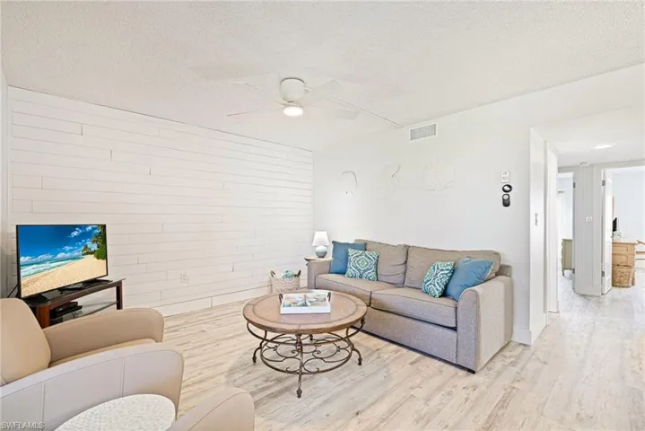 Living area featuring wood finished floors, a textured ceiling, a ceiling fan, and wooden walls