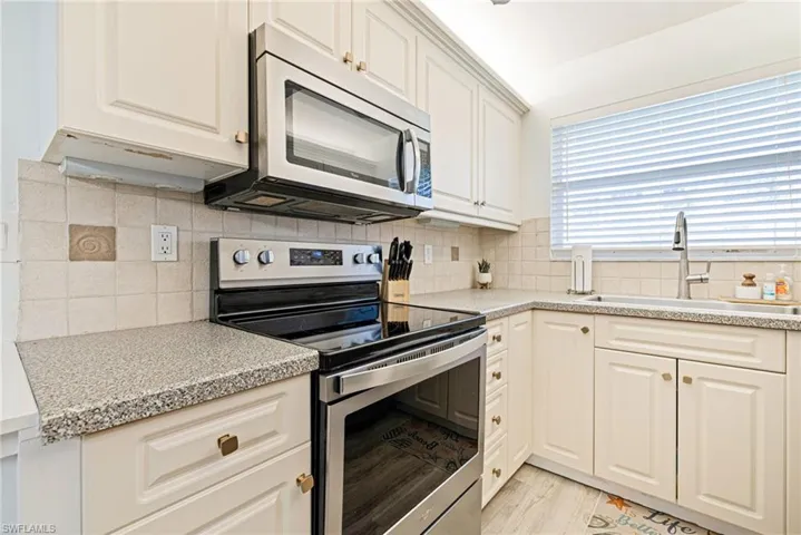 Kitchen featuring stainless steel appliances, backsplash, light stone countertops, white cabinets, and light wood-style flooring