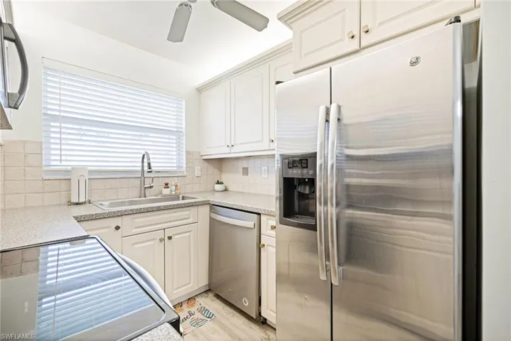 Kitchen featuring appliances with stainless steel finishes, backsplash, white cabinets, light wood-style floors, and light stone counters