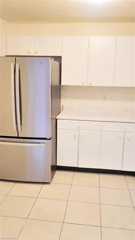 Kitchen with freestanding refrigerator, white cabinets, and light tile patterned floors