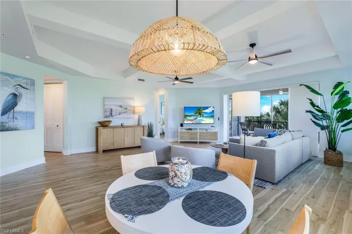 Dining space with wood finished floors, a ceiling fan, coffered ceiling, beamed ceiling, and a raised ceiling