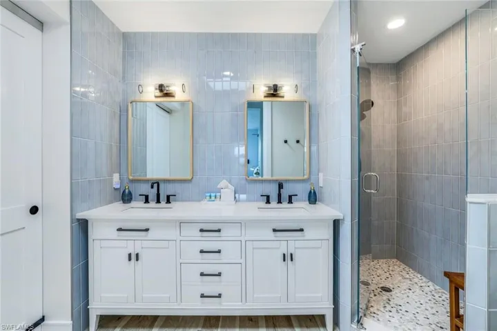 Bathroom featuring tile walls, double vanity, a stall shower, backsplash, and light wood-type flooring