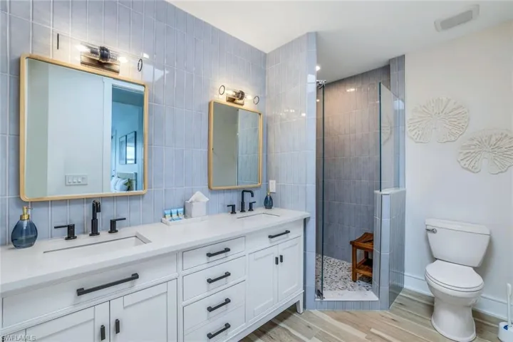 Bathroom with tile walls, double vanity, walk in shower, and light wood finished floors