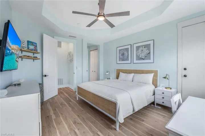 Bedroom with a raised ceiling, light wood finished floors, a closet, and ceiling fan